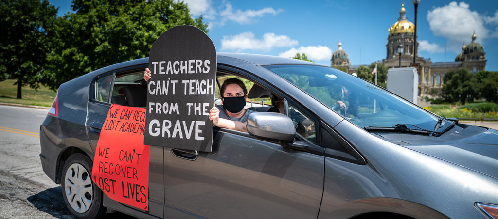 Person in car with sign that says "tTeachers can't teach from the grave."