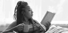 Black woman holding a coffee mug and reading a book while in a reclined position