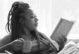 Black woman holding a coffee mug and reading a book while in a reclined position