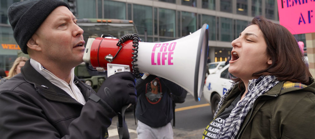 Man with bullhorn that says pro-life on it screaming at woman at anti abortion protest
