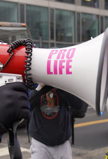 Man with bullhorn that says pro-life on it screaming at woman at anti abortion protest