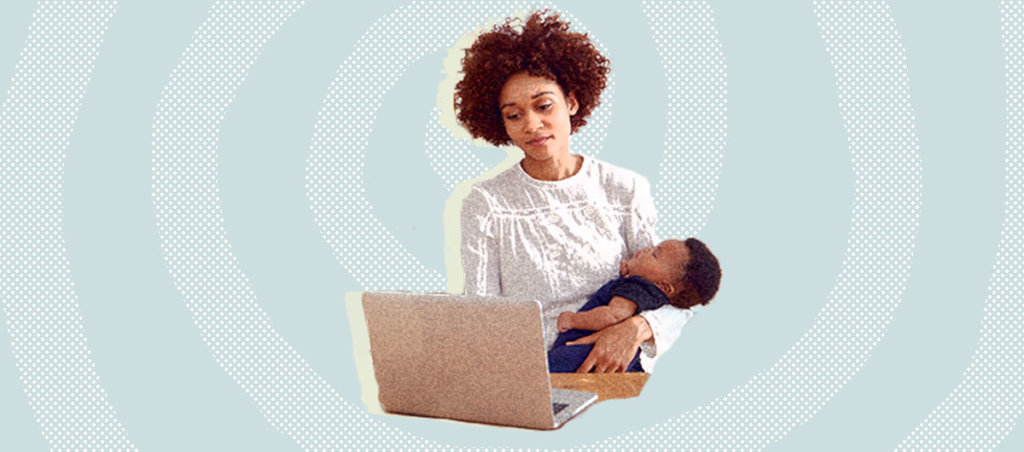 Black mother working in front of laptop while cradling an infant