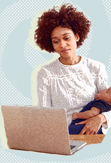 Black mother working in front of laptop while cradling an infant