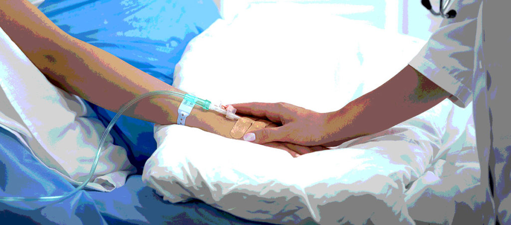 A doctor holding the hand of a woman who is lying in a hospital bed