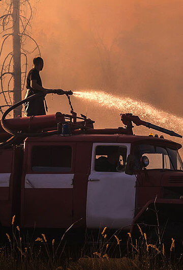 Person on a truck with a hose fighting back wildfire with water