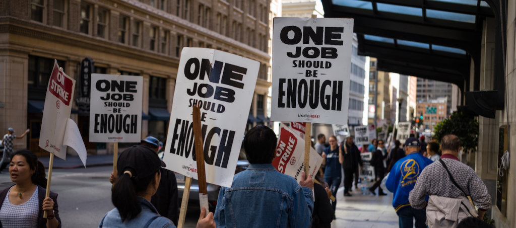 Workers picketing with signs that say one job is not enough