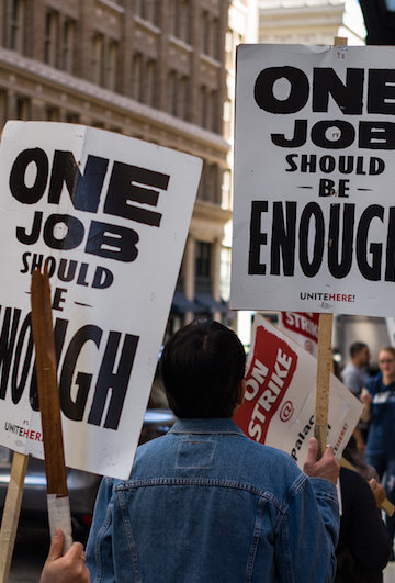 Workers picketing with signs that say one job is not enough