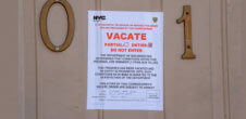 A sign on a door from NYC Buildings that says "Vacate: The Department of Buildings Has Determined that conditions within these premises are imminently perilous to life. This premises has been vacated and rrentry is prohibited until such conditions has been eliminated to the satisfaction of the department. Violators of the commissioner's vacate order are subject to arrest."