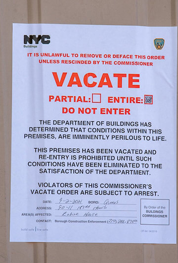 A sign on a door from NYC Buildings that says "Vacate: The Department of Buildings Has Determined that conditions within these premises are imminently perilous to life. This premises has been vacated and rrentry is prohibited until such conditions has been eliminated to the satisfaction of the department. Violators of the commissioner's vacate order are subject to arrest."