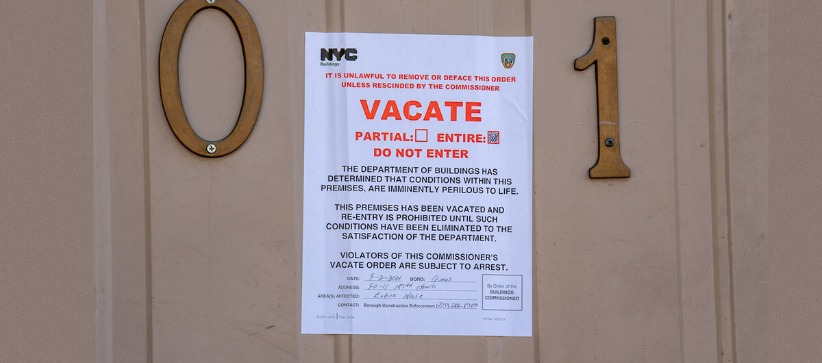 A sign on a door from NYC Buildings that says "Vacate: The Department of Buildings Has Determined that conditions within these premises are imminently perilous to life. This premises has been vacated and rrentry is prohibited until such conditions has been eliminated to the satisfaction of the department. Violators of the commissioner's vacate order are subject to arrest."