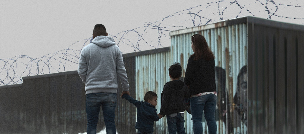 A family stands in front of the USA Mexico Border wall