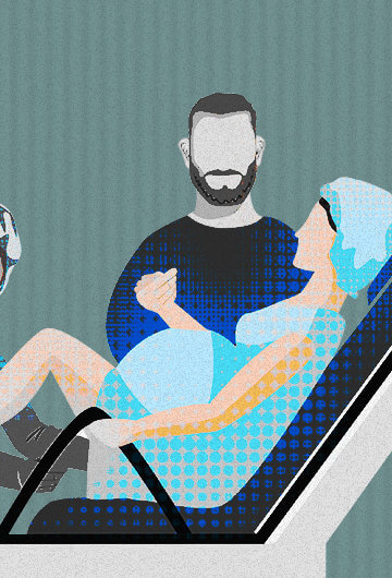 A pregnant person in on a hospital chair getting examined by a health professional. A man is holding their hand.