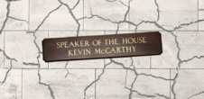 The speaker of the house sign on a grey crackled background. the sign itself reads speaker of the house kevin mccarthy.
