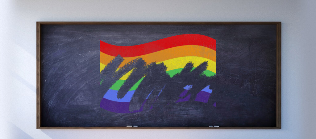 Image of a LGBTQ flag on a school blackboard. The flag is being erased as if it were drawn in chalk.