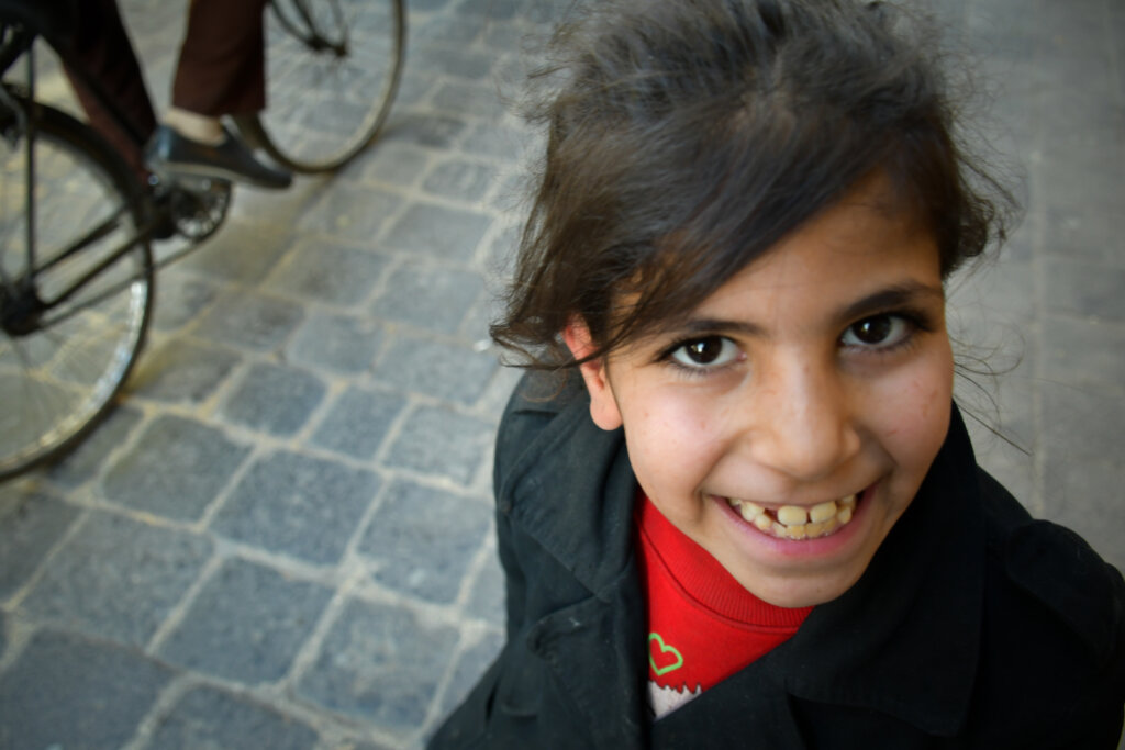 A young girl with dark hair smiling, looking up at the camera